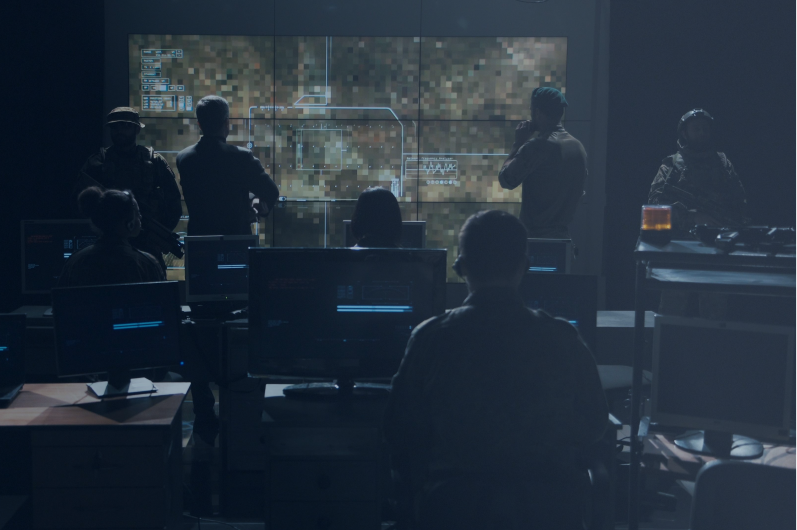 Dark command center with analysts and uniformed personnel at workstations viewing a large digital map — government-grade critical capability.